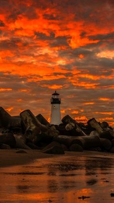 a light house sitting on top of a sandy beach next to the ocean at sunset