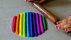 a woman's hands holding a wooden rolling pin with rainbow colors on it