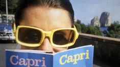 a woman wearing sunglasses reading a book with the caption capri in front of her