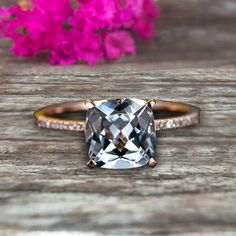 an engagement ring with a cushion cut diamond in the center on a wooden table next to pink flowers