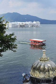 a red boat traveling across a lake next to a tall white building with a roof