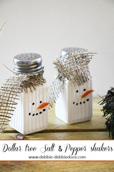 three snowmen made out of white boxes sitting on a wooden table next to plants