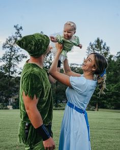 a woman holding a baby up to her face while standing next to a man in a costume