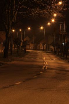 an empty street at night with lights shining on the trees and houses in the background