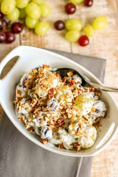 a white bowl filled with grapes and nuts next to a spoon on top of a napkin