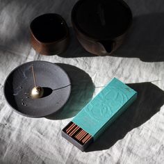 a box of matches sitting on top of a table next to two bowls and a candle