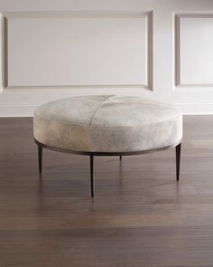 a round ottoman sitting on top of a hard wood floor next to a white wall