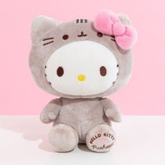 a gray hello kitty stuffed animal with a pink bow on it's head sitting in front of a pink background