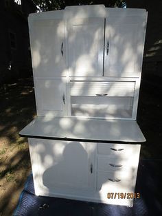 a white cabinet sitting on top of a blue mat in front of a tree and house