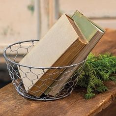 an open book sitting in a wire basket on top of a wooden table next to a plant