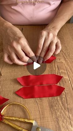 a person cutting out red ribbon on top of a wooden table next to some scissors