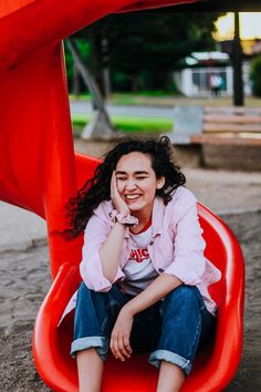 a woman sitting on top of a red slide in a playground area with her hands to her face