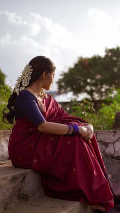 a woman in a red sari sitting on a stone wall and looking off into the distance