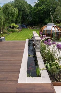 a wooden deck next to a small pond with flowers and plants growing on the side