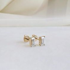 two diamond stud earrings sitting on top of a white surface