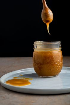 a spoon is lifting some honey from a glass jar on a white plate with a black background