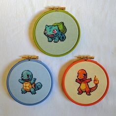 three cross - stitch hoops with different designs on them sitting on a white surface