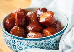 a blue and white bowl filled with cooked meat on top of a wooden table next to a napkin