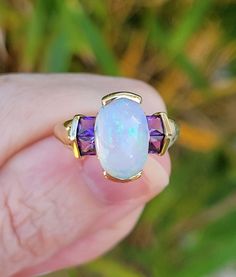 Absolutely stunning vintage 14k gold opal and amethyst ring, size 6-1/4. Very colorful opal dances with fire and is surrounded by four square princess cut channel set purple amethysts, a dramatic color contrast! Measures 1/2" north/south. Hallmarked "14k" on the inside of the ring shank. Weighs 3.2 grams. Opal measures 12mm x 8mm, amethysts each measure 4mm square. In exceptional extremely well cared for condition, circa 1990s.  On the fence about something you see on our web site today? We welcome you to read our reviews! https://www.etsy.com/shop/SundayandSunday/reviews OUR RETURN/REFUND POLICY: If you wish to return an item, you MUST notify us within the allowable THREE (3) DAY INSPECTION PERIOD after you receive it. We will refer to the USPS delivery confirmation (tracking) date that w Elegant Multi-stone Opal Gemstones, Fine Jewelry Opal And Moonstone Multi-stone Ring, Fine Jewelry Multi-stone Opal Jewelry, Multi-stone Opal Fine Jewelry, Opal And Moonstone Multi-stone Fine Jewelry Ring, Oval Opal Jewelry Collectible, Opal Multi-stone Fine Jewelry, Collectible Oval Opal Jewelry, Fine Jewelry Opal Ring With Multi-stone Round Cut