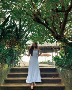 a woman in a white dress is standing on some steps and looking up at the sky