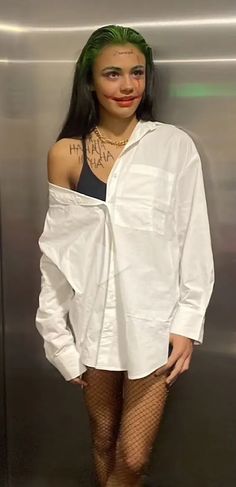 a woman with green hair and tattoos standing in front of a metal wall wearing a white shirt