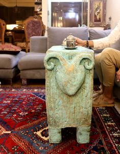 a man kneeling down next to a green vase on top of a rug in a living room