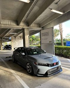 a grey car parked under an overpass in a parking lot with other cars behind it