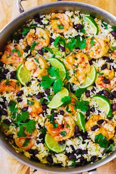 a skillet filled with rice, black beans and limes on top of a wooden table