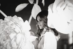 black and white photograph of woman with large flower in foreground, looking at camera