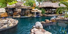 an outdoor swimming pool surrounded by rocks and palm trees, with a waterfall in the middle