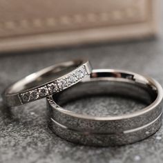 two white gold wedding rings sitting on top of a gray table next to each other