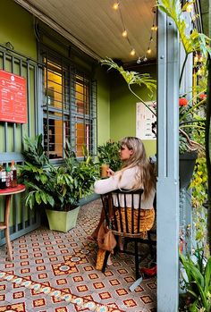 a woman sitting at a table with potted plants on the outside of a building