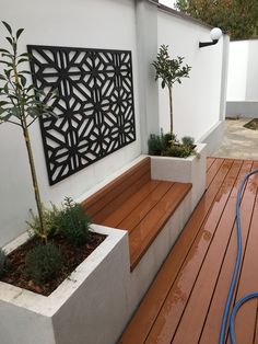 a wooden deck next to a white wall with a planter and tree on it