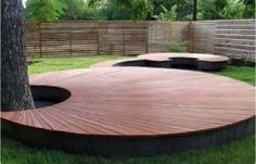 a wooden deck in the middle of a grassy area next to a tree and fence