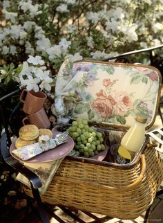 a wicker picnic basket filled with food and wine on a patio table next to white flowers