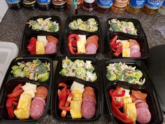 six black plastic trays filled with different types of food on top of a counter