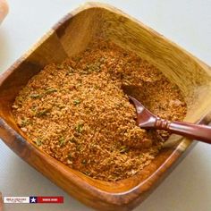 a wooden bowl filled with spices next to a person's hand holding a spoon