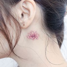 a woman's neck with a small pink flower tattoo on the back of her neck