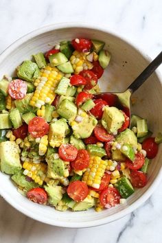 a white bowl filled with corn, avocado and tomatoes