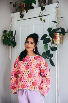 a woman standing in front of a white door wearing a pink and yellow crochet sweater