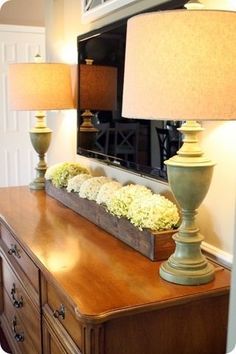 an image of a dresser with flowers on it and a large tv in the background