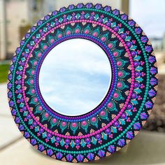 a circular mirror with an intricate design on the front and back side is shown in purple, blue, and pink