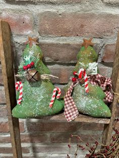 two green christmas trees sitting on top of a wooden chair next to a brick wall