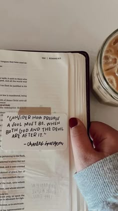 a person's hand on top of an open book next to a cup of coffee