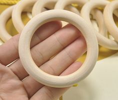 a hand holding a small wooden ring in front of some other wood rings on a table