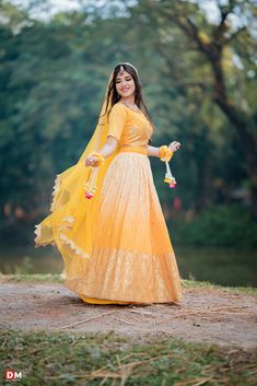 a woman in yellow dress holding flowers and posing for the camera with trees in the background