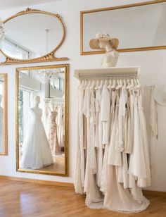 wedding gowns and dresses hanging in front of a mirror on the wall next to a dress rack