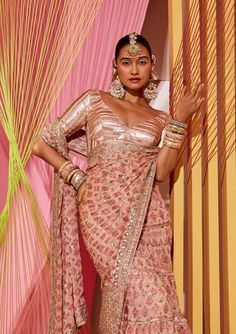 Editor's Note A delicate, floral jaal, on soft flowing georgette in rose blush pink, embellished in exquisite gota and dori. This easy wrap, layered frill sari with flounce and flow, has delicate buttis with a rich, intricate embroidered border. The blouse in tonal gold geometric gota, cut with classic elbow sleeves adds glam this and glitz to the ensemble. Fabric: Blouse: tussar, sari: georgette Color: Pink Component: Sari and blouse Occasion: Festive Note: Product colour may slightly vary due Festive Pink Pre-draped Saree With Mirror Work, Pink Wedding Pre-draped Saree, Pink Pre-draped Saree With Sheer Dupatta For Transitional Season, Pink Chinon Pre-draped Saree For Navratri, Glamorous Pink Pre-draped Saree With Mirror Work, Georgette Pre-draped Saree With Gota Work For Reception, Peach Pre-draped Saree For Wedding, Elegant Pink Pre-draped Saree For Reception, Pink Pre-draped Saree With Mirror Work