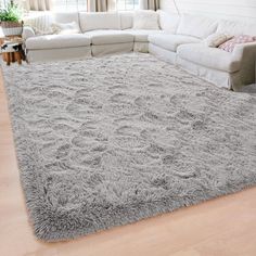 a living room with a large gray rug on the floor and white couches in front of it