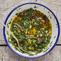 a bowl filled with soup and greens on top of a wooden table next to a spoon